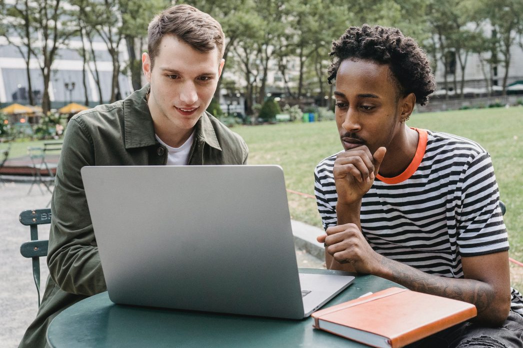 Two students looking at a laptop in a park